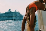 Woman rests with legs up the wall of a cruise ship balcony while another cruise ship is off in the distance.