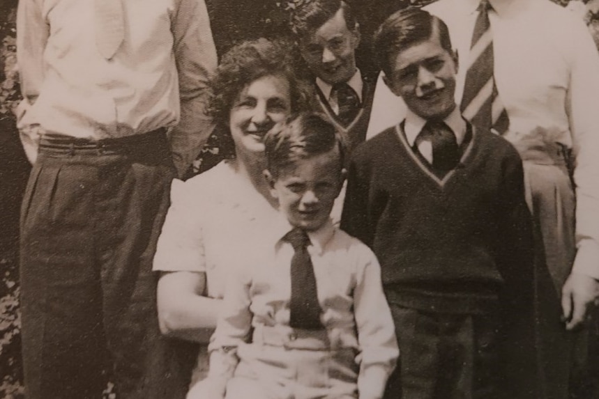 Black and white photo of seated woman smiling with young child on her lap and two other young boys nearby. All smile and squint.