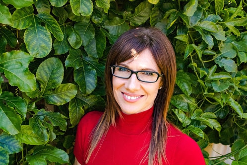 A woman smiles for the camera posing for a photo in front of a tree.