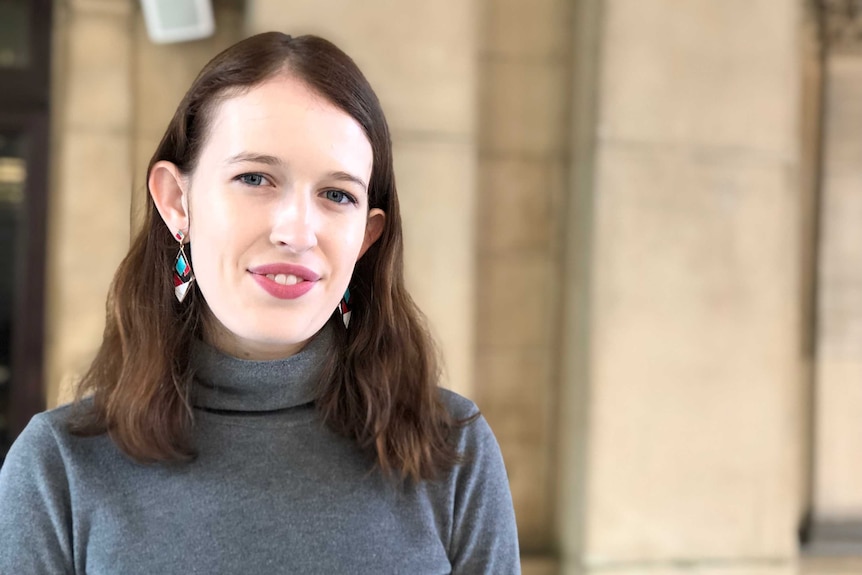 Amelia Morris, a young woman with brown hair, a grey top and colourful earrings.