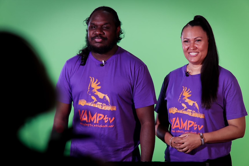 two teachers wearing purple t-shirts in front of a green screen