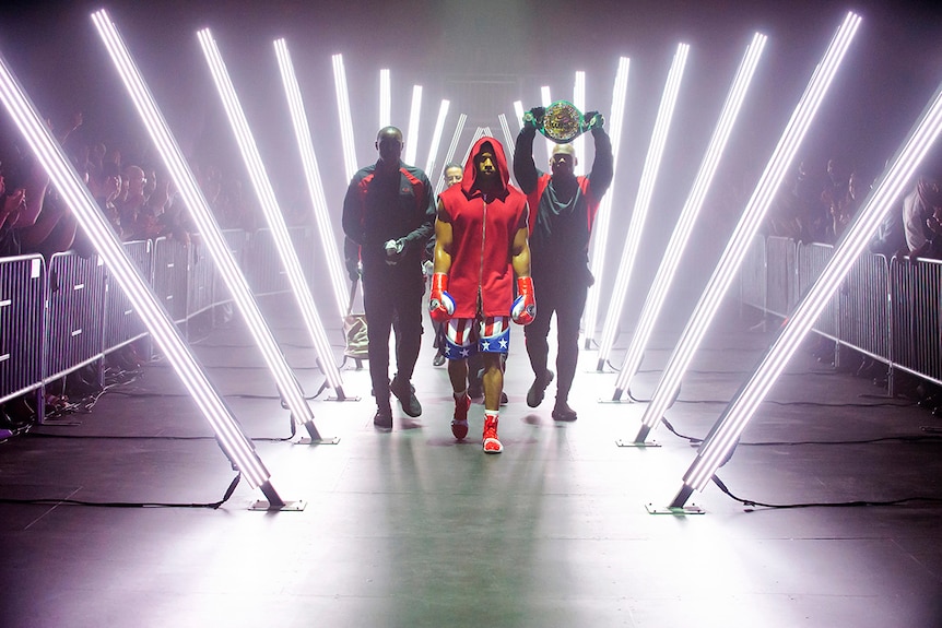 Colour still of Michael B Jordan and posse walking between neon lights in 2018 film Creed II.