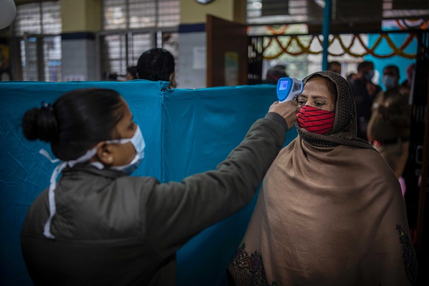 An Indian health worker checks the body temperature of a woman