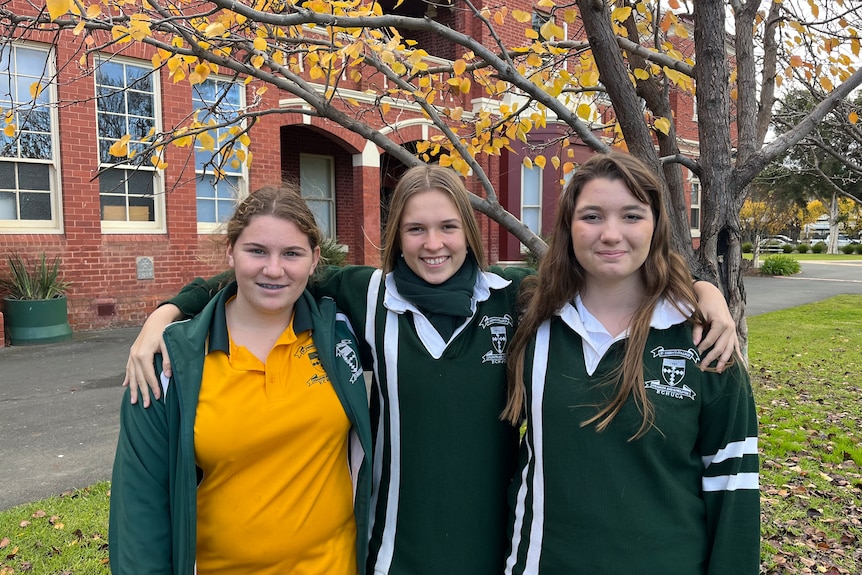 Three smiling girls in school uniforms.