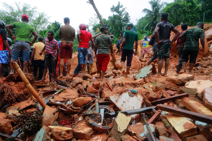 Villagers stand on debris of a house destroyed in a landslide.