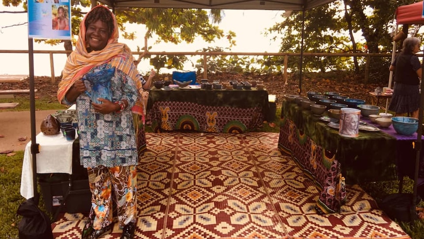 A woman stands smiling in a colourful market stall.