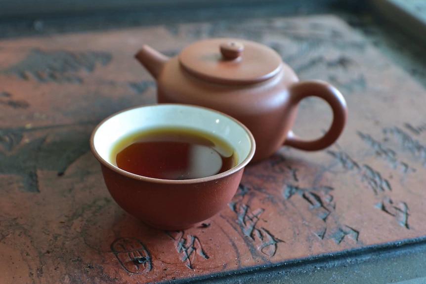 A teapot and cup rest on a tray etched with Chinese characters