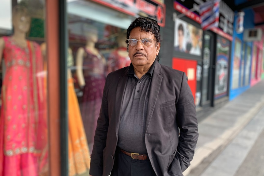 Man in a suit walks down a street in front of a sari shop and hairdresser.