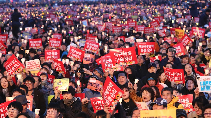 Hundreds of people holding candles and banners reading Park Guen-Hye's arrest