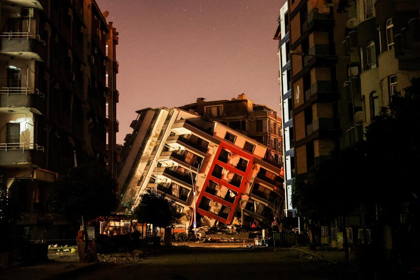 A partially-collapsed building framed by two large buildings in Antakya, Türkiye.