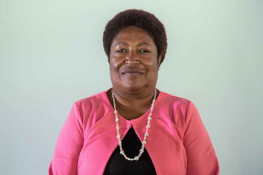 A woman with dark brown afro hair wearing a pink jacket smiling