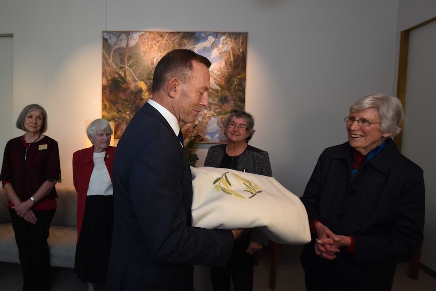 Prime Minister Tony Abbott receives the blanket by the ACT Embroiderers Guild at Parliament House.