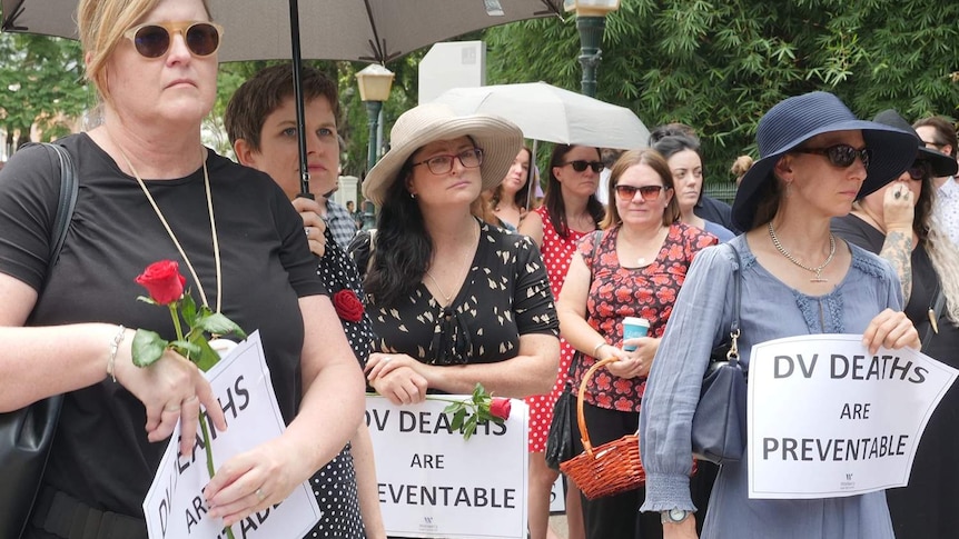 People holding signs at a Red Rose rally against domestic violence outside Parliament House in Brisbane.