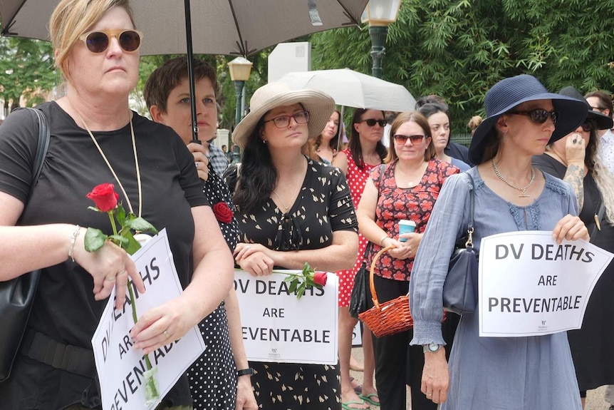 People holding signs at a Red Rose rally against domestic violence outside Parliament House in Brisbane.