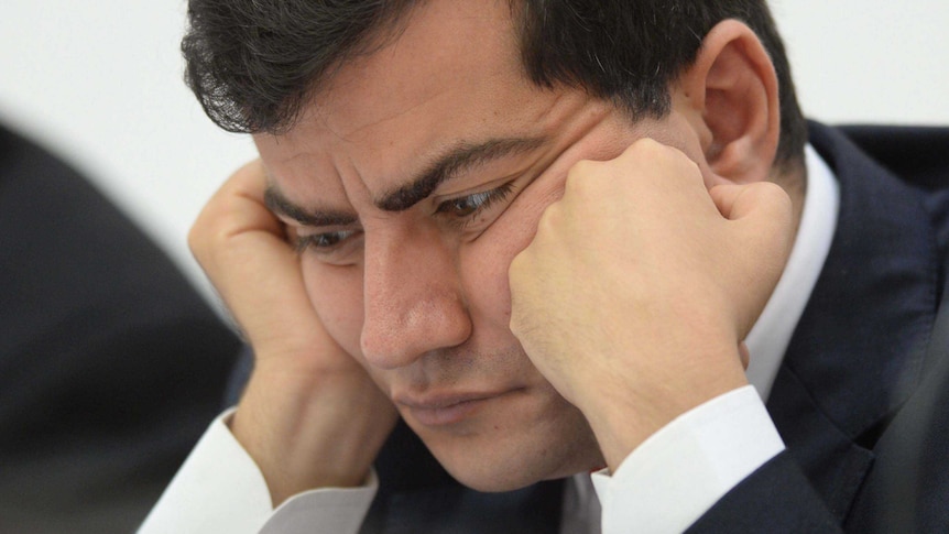 Labor Senator Sam Dastari sits with his face resting on his hands during Senate Hearings, looking concerned and deep in thought.