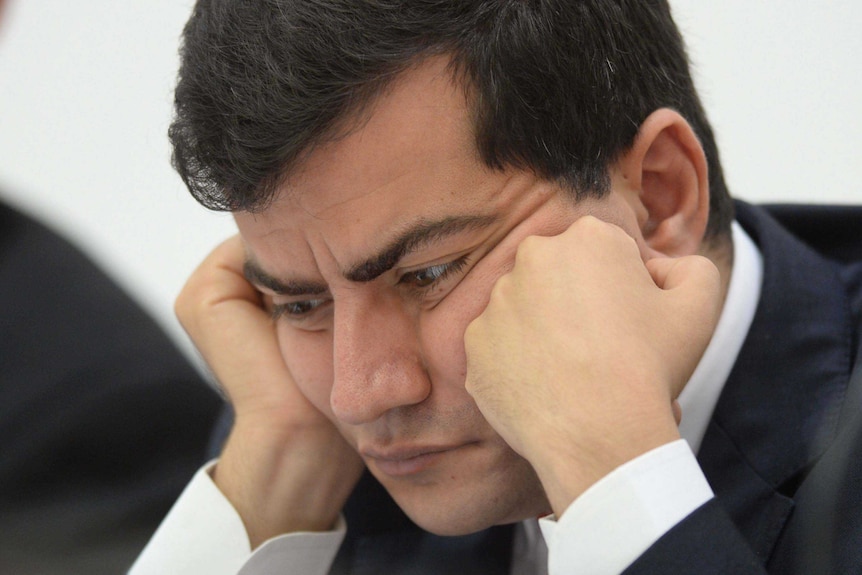 Labor Senator Sam Dastari sits with his face resting on his hands during Senate Hearings, looking concerned and deep in thought.