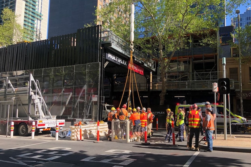 Workers in high-visibility jackets gather at the site to plan a rescue of the crane driver.