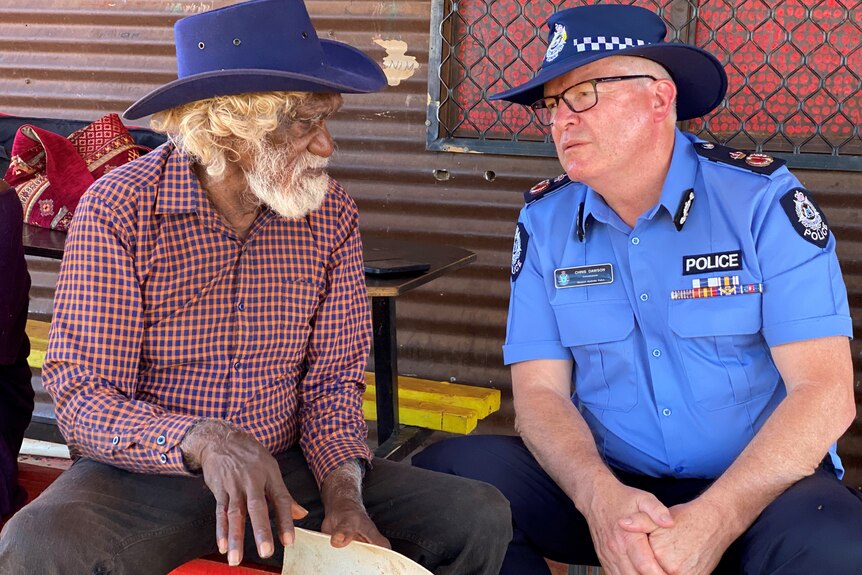 An elderly Indigenous man and a police officer sit talking.