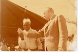 A sepia tinted photo of Gough Whitlam pouring a handful of sand into Vincent Lingiari's hand.