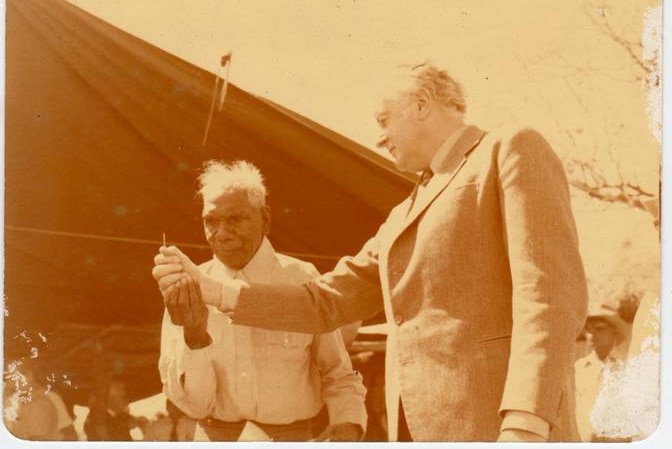 A sepia-tinted photo of Gough Whitlam pouring a handful of sand into Vincent Lingiari's hand.