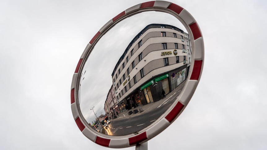 A circular mirror reflects a three-storey building on a quiet street