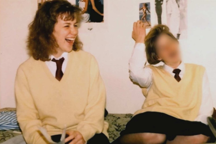 two school girls sit on bed together.