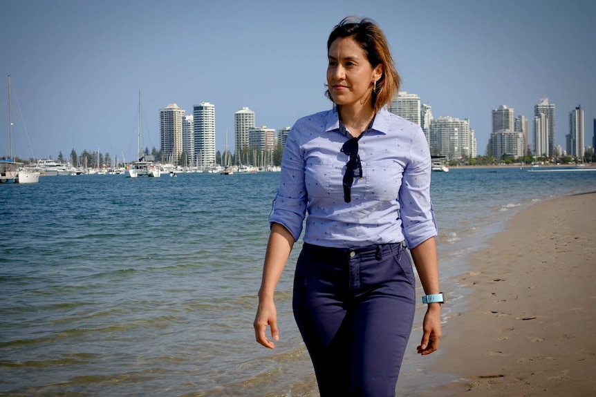 Silvia Martinez walks along a Gold Coast beach with high-rise buildings in the background.