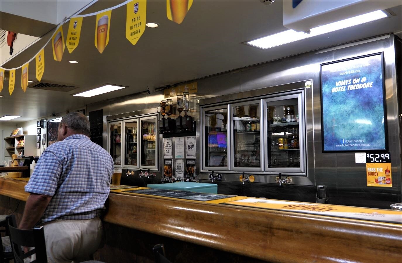 A man facing away leans against the bar next to a freshly poured schooner. He's standing alone.