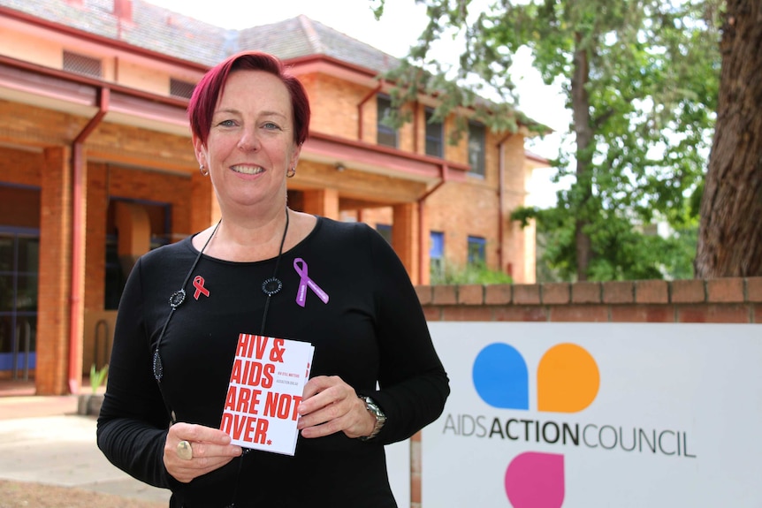 AIDS Action Council of the ACT executive director Phillippa Moss hold a book called HIV and AIDS are not over.