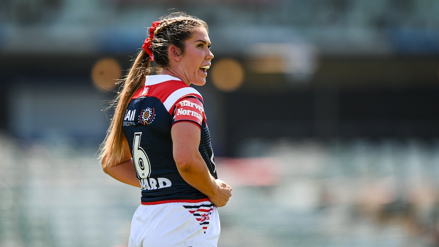 Charlotte Caslick stands and grimaces, looking off to one side wearing a dark blue number 6 jersey