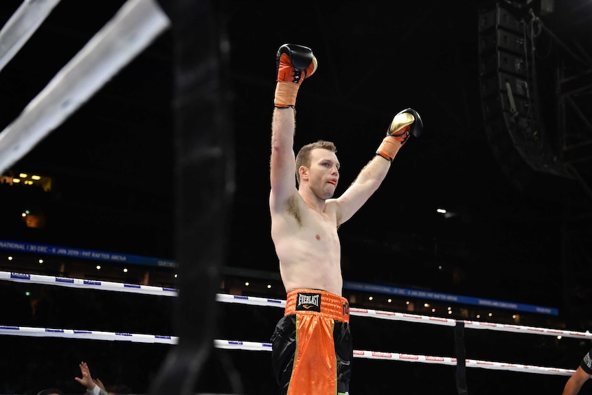 Jeff Horn raises his black and gold gloves while standing in a boxing ring.