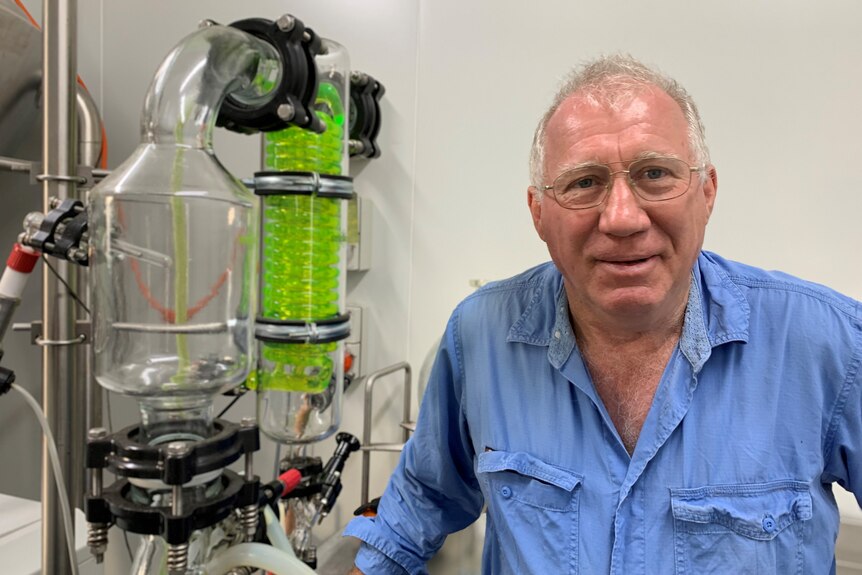 Man in blue shirt posing beside a green glass scientific tube in a lab.