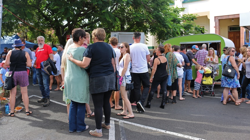 A crowd of people lining up to order a beer from a small green van.