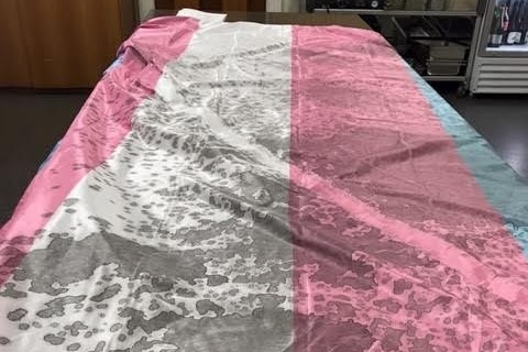 Pink, blue and white striped flag lying on a table splattered with a black substance 