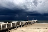 Black storm sky near a coastal jetty.