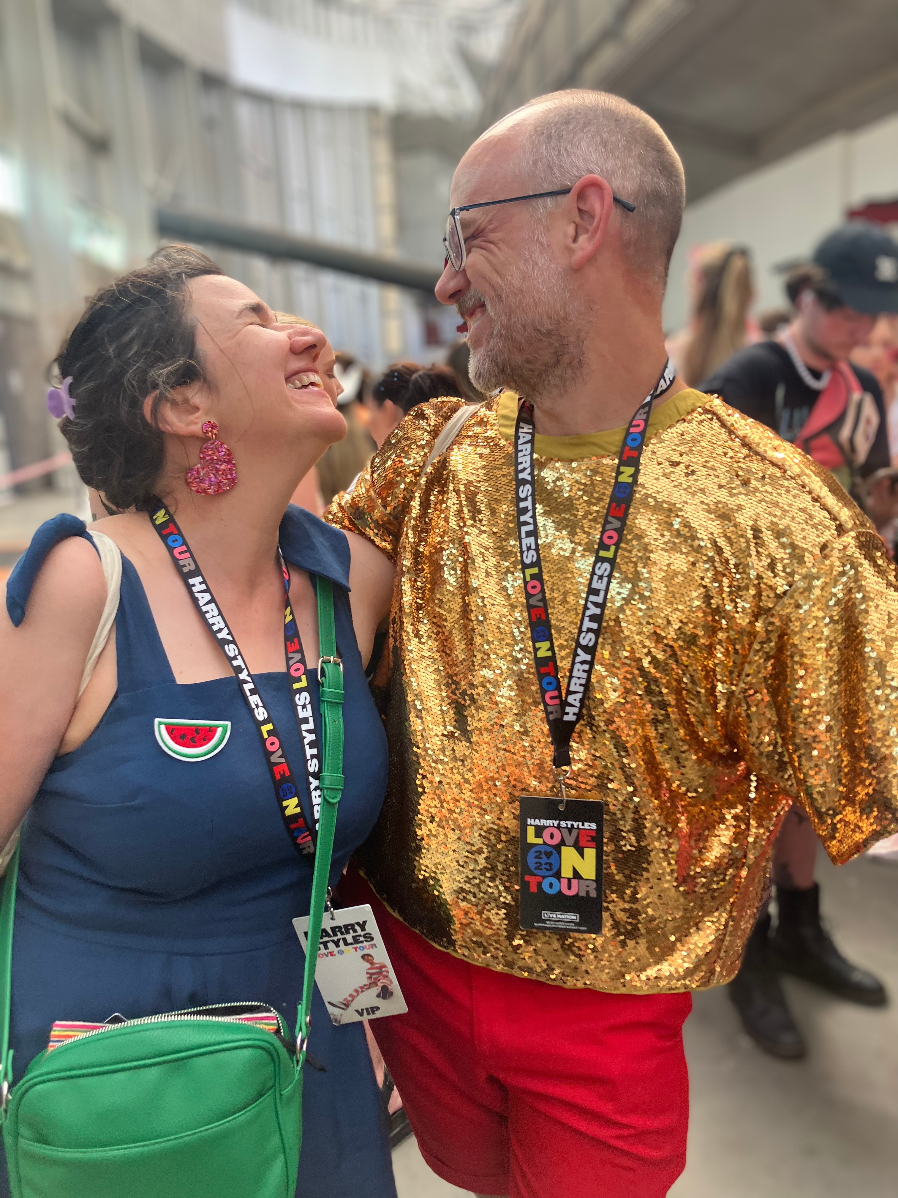 A woman in a blue dress grins at a man in a sequined gold shirt.