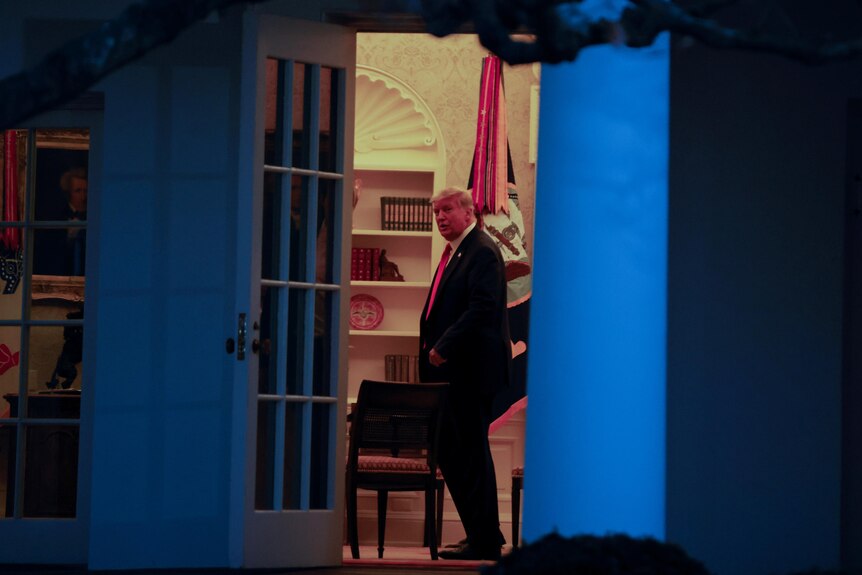 Donald Trump stands in the doorway of the White House at night 