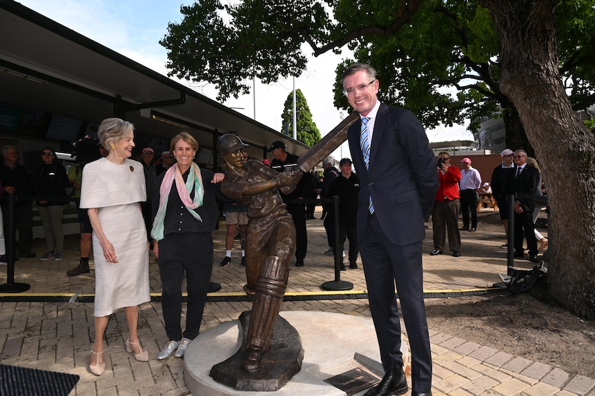 Three people standing next to a bronze sculpture of a female cricketer