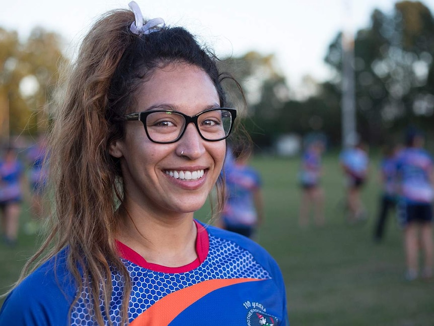 A close-up of a women with glasses smiling at camera. Her team playing in the background.
