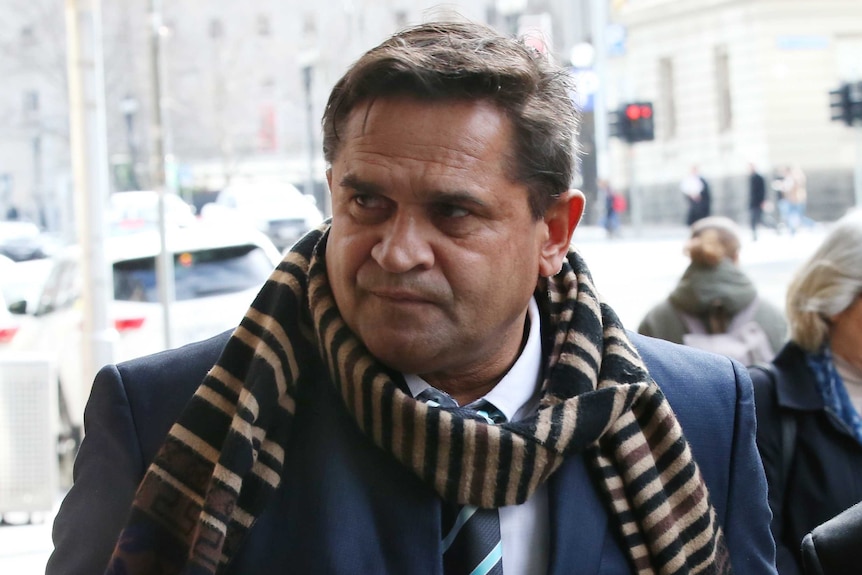 Nicky Winmar, dressed in a suit and tie and with a scarf around his neck, walks outside court.