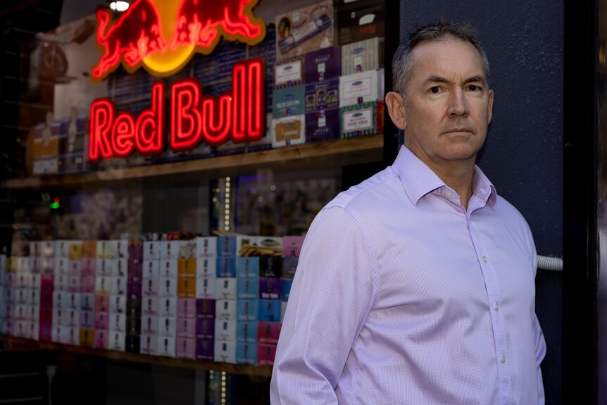 Man wearing blue shirt standing in front of a convenience store with a Red Bull logo behind him.