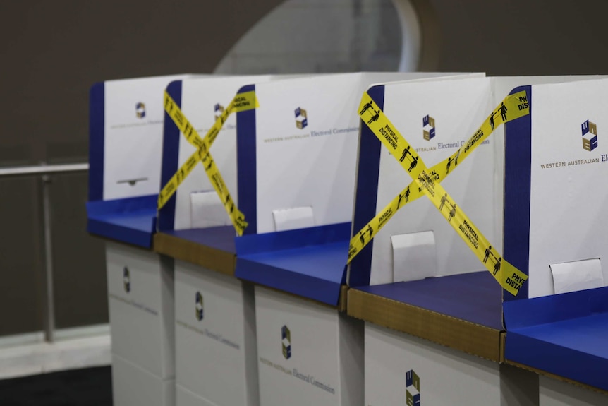 Four cardboard voting booths for the WA election with every second one covered by yellow tape that says 'physical distancing'