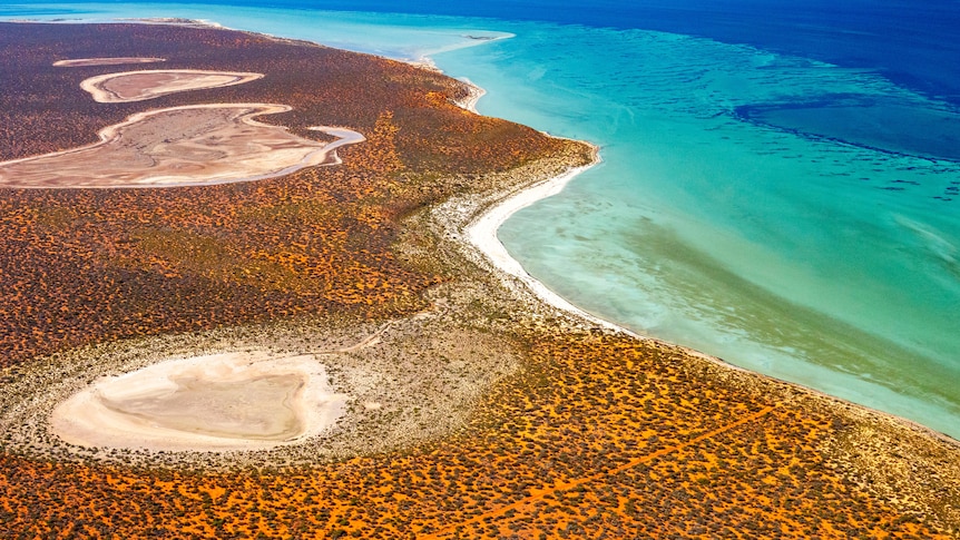 An aerial photo of a section of coastline with bright blue water and red dirt. 