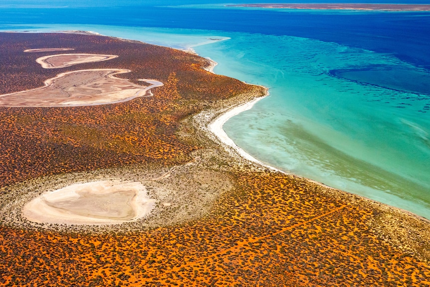 An aerial photo of a section of coastline with bright blue water and red dirt. 