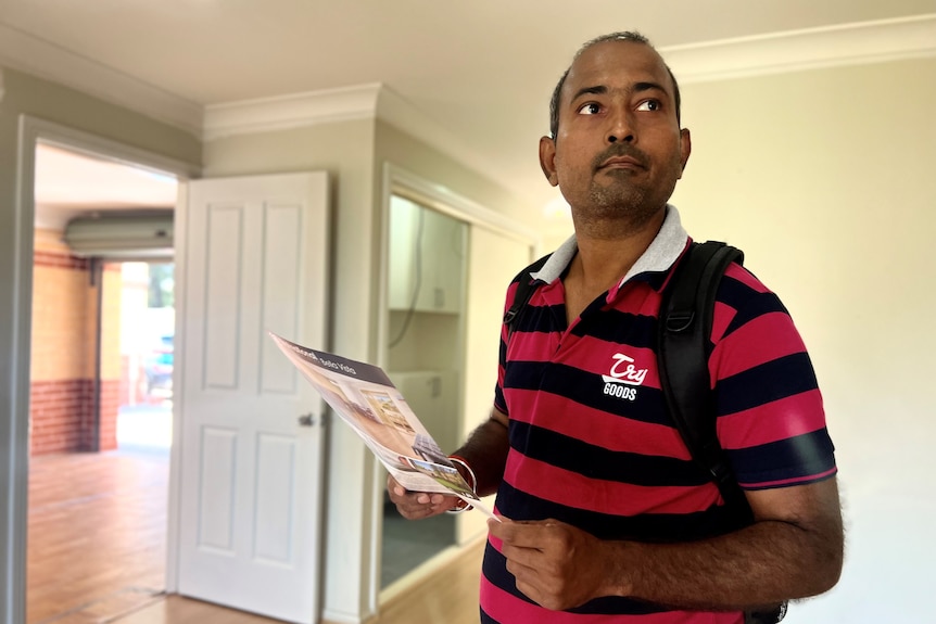 Man inspects an open house, holding brochure.