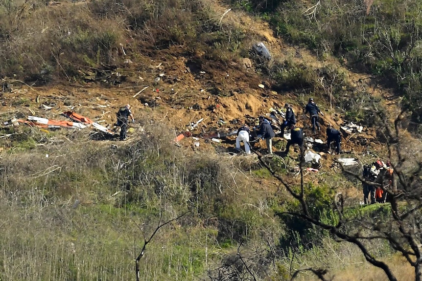 People in uniform work through debris on a rugged hillside.