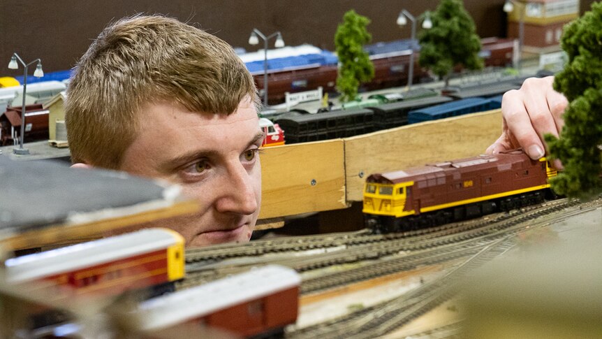 A man placing a model railway train engine onto a miniature track.