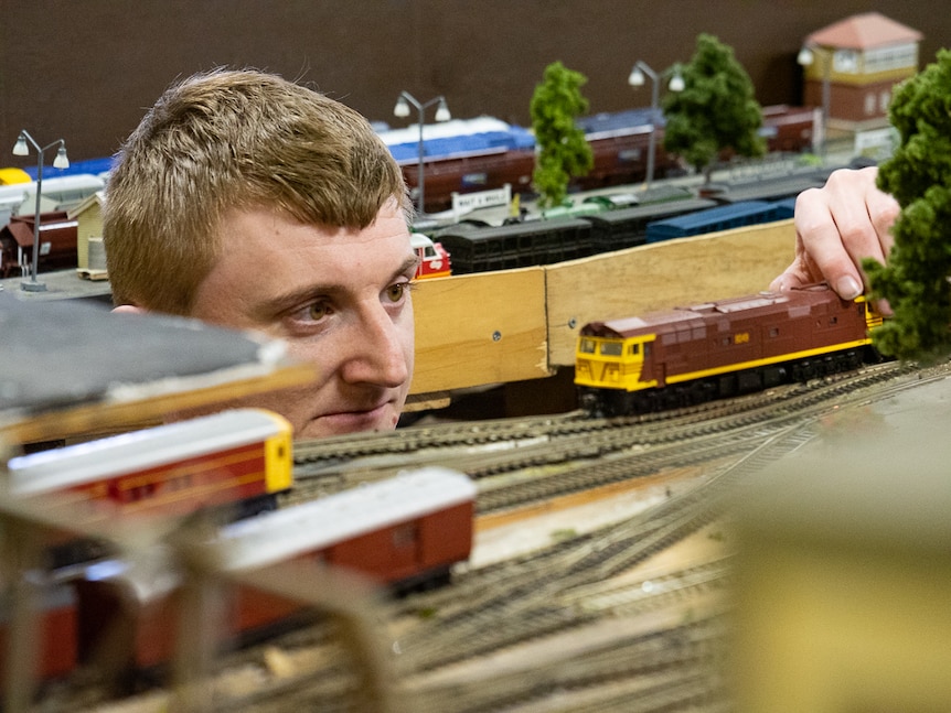 A man placing a model railway train engine onto a miniature track.