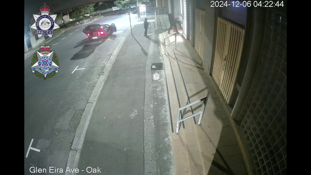 A screengrab from CCTV of a road with a car and people standing at the entrance of a building