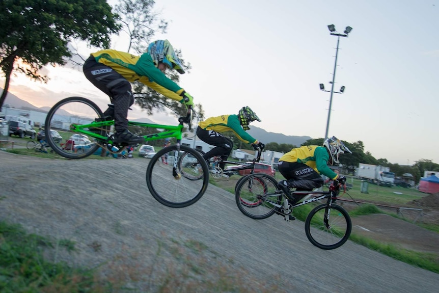 Three riders glide through the air after jumping their bmx bikes over a mound